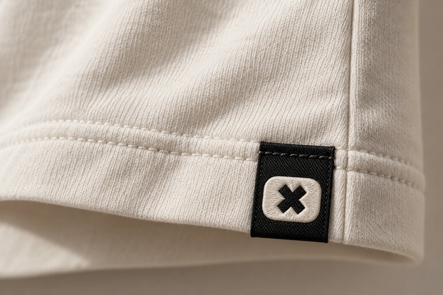 Small black seam label on a bone T-shirt, embroidered with the amsteltown o and one St Andrew’s cross